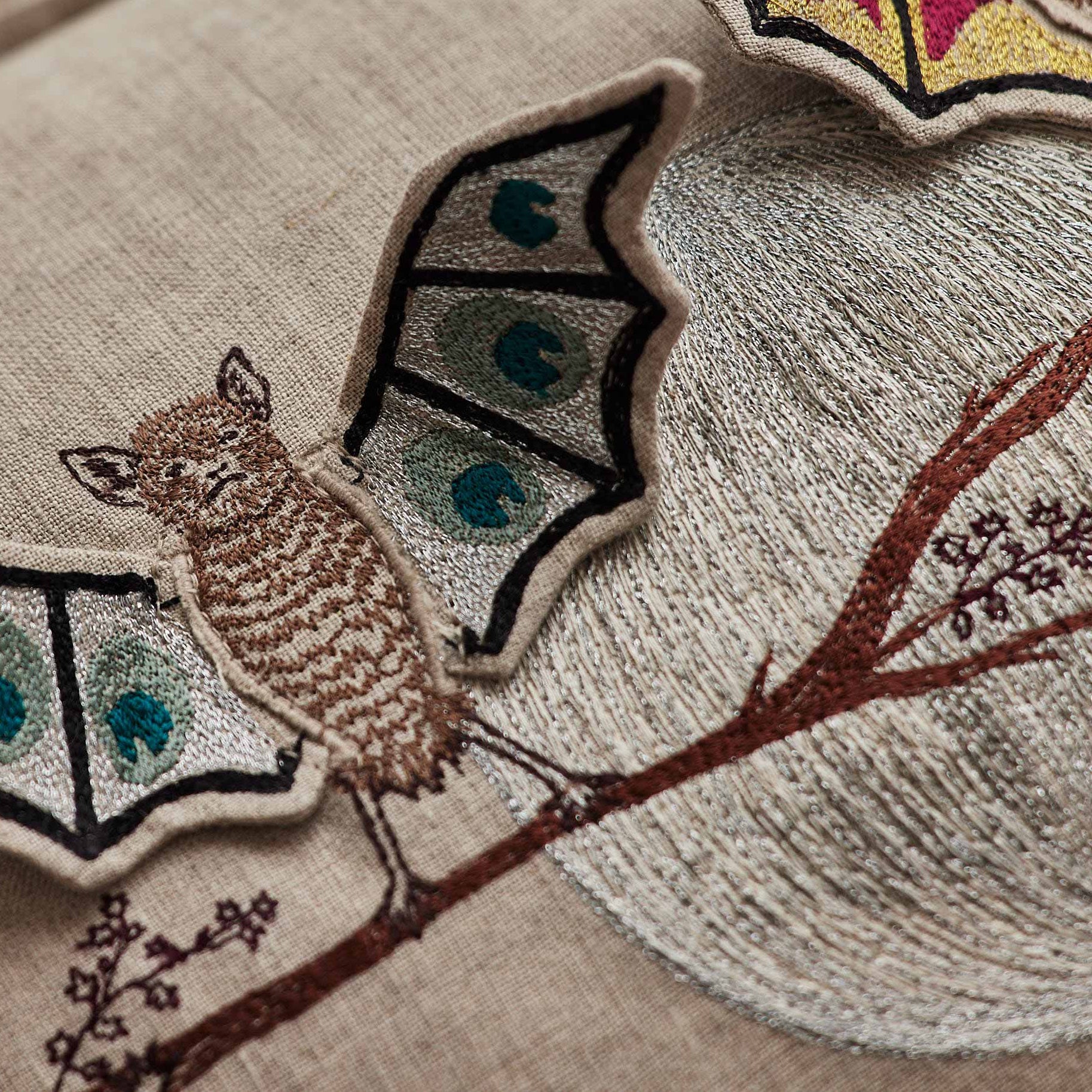 Coral and Tusk’s “Bat Branch” embroidered linen pillow featuring three bats hanging from a maple tree branch