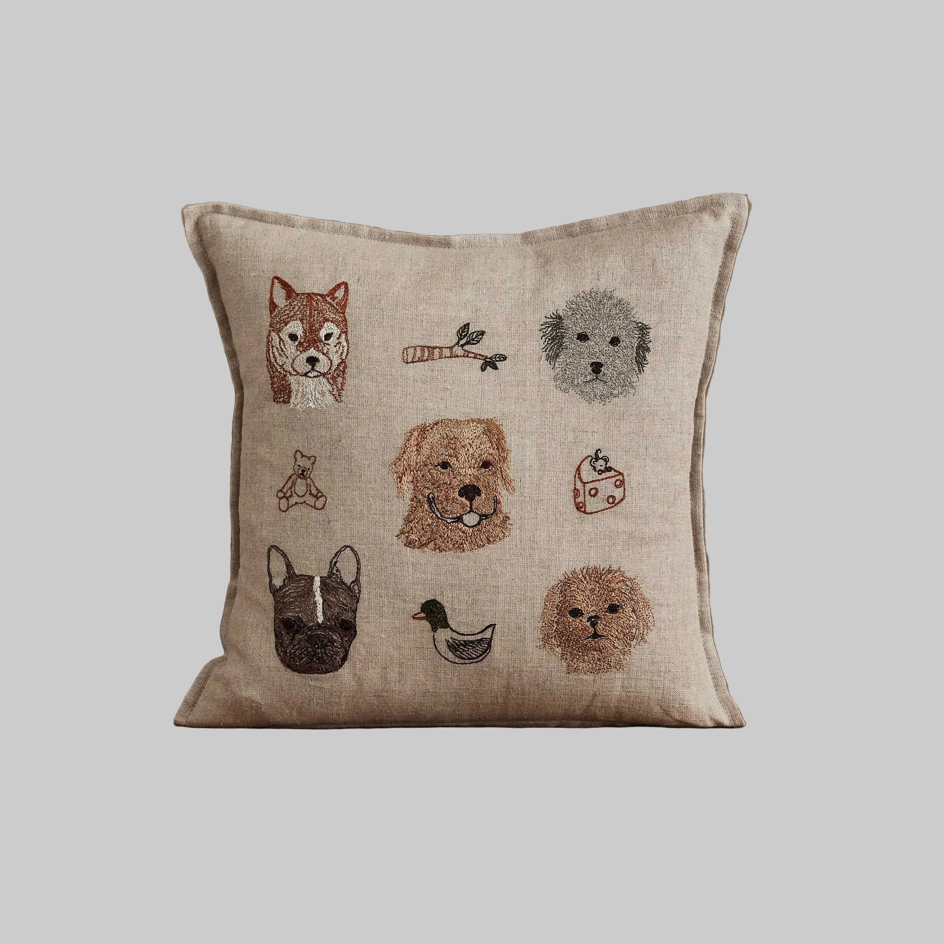 Coral and Tusk’s “Charming Canines” embroidered linen pillow featuring designs of several dog breeds and their toys, measures 12” x 12”