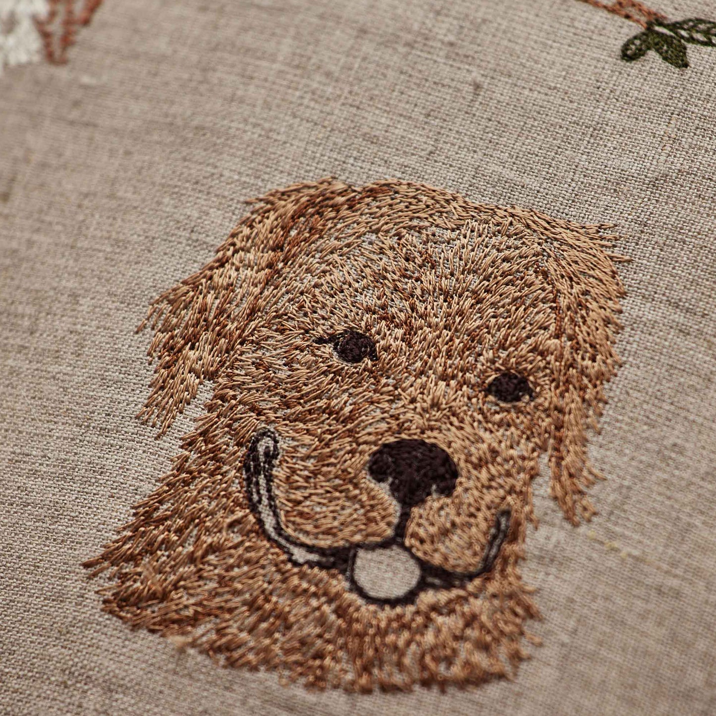 Coral and Tusk’s “Charming Canines” embroidered linen pillow featuring designs of several dog breeds and their toys, measures 12” x 12”