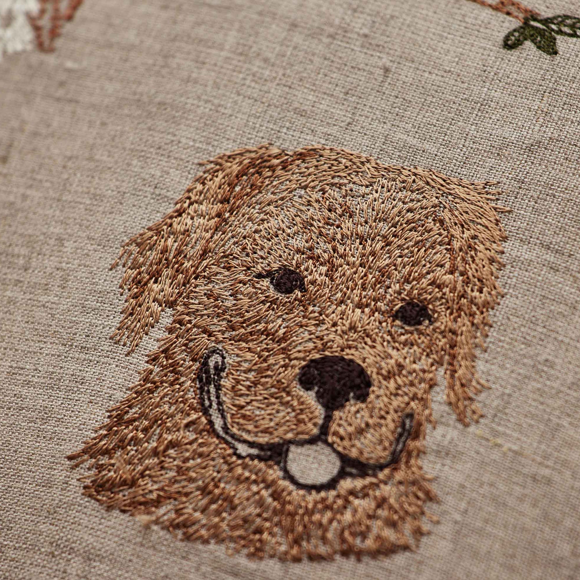 Coral and Tusk’s “Charming Canines” embroidered linen pillow featuring designs of several dog breeds and their toys, measures 12” x 12”