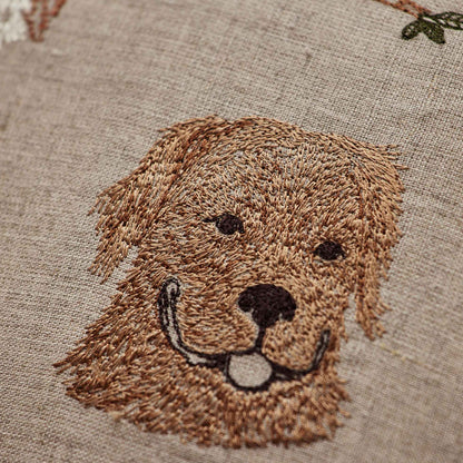 Coral and Tusk’s “Charming Canines” embroidered linen pillow featuring designs of several dog breeds and their toys, measures 12” x 12”