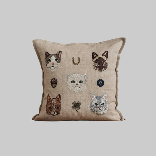 Coral and Tusk’s “Charming Cats” embroidered linen pillow featuring five cats and their lucky charms, measures 12” x 12”