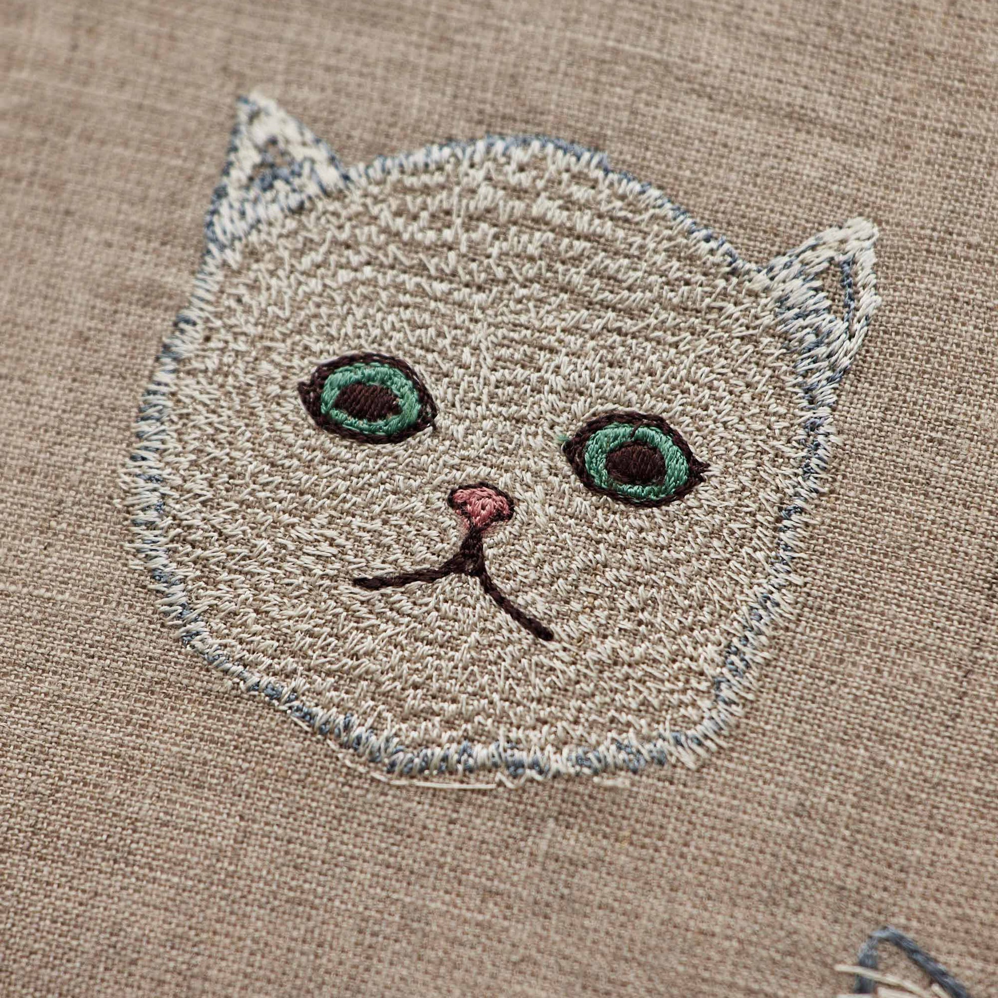 Coral and Tusk’s “Charming Cats” embroidered linen pillow featuring five cats and their lucky charms, measures 12” x 12”