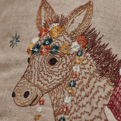 Coral and Tusk’s “Christmas Donkey” embroidered linen pillow featuring a  fox dressed up as Santa riding in on a festively-adorned donkey, measures 16” x 16”