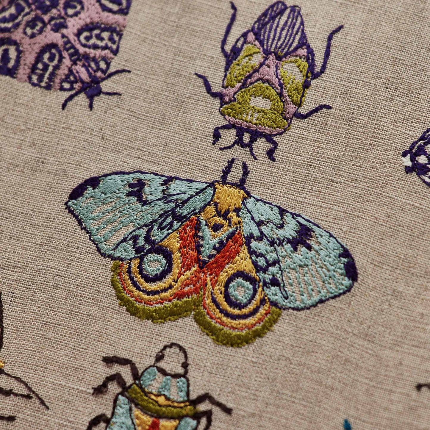 Coral and Tusk’s “Fancy Flight” embroidered linen pillow featuring colorful depictions of moths and beetles, measures 12” x 16”