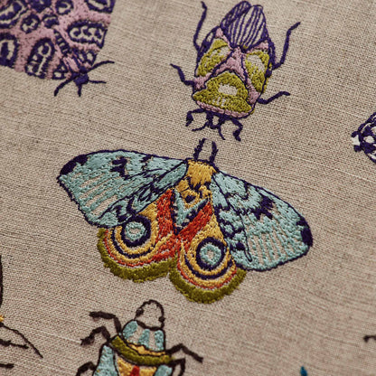 Coral and Tusk’s “Fancy Flight” embroidered linen pillow featuring colorful depictions of moths and beetles, measures 12” x 16”