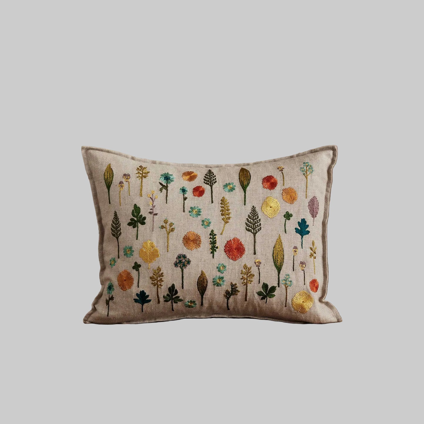 Coral and Tusk’s “Small Garden” embroidered linen pillow featuring a field of dandy flowers, forget-me-nots, violets, and sprigs, measures 12” x 16”