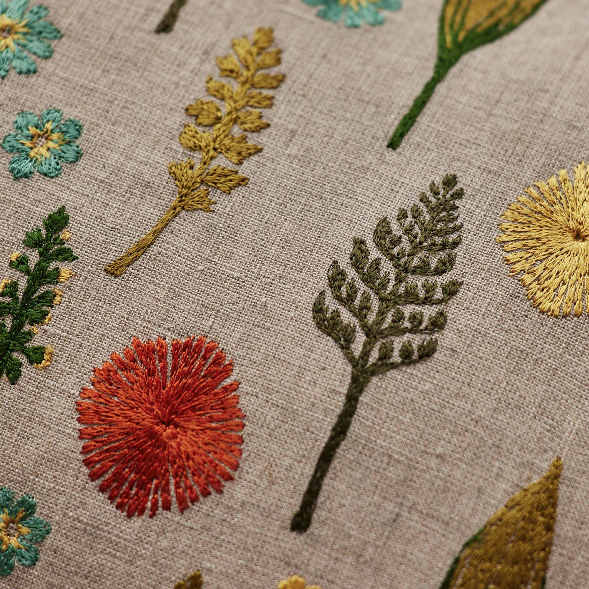 Coral and Tusk’s “Small Garden” embroidered linen pillow featuring a field of dandy flowers, forget-me-nots, violets, and sprigs, measures 12” x 16”