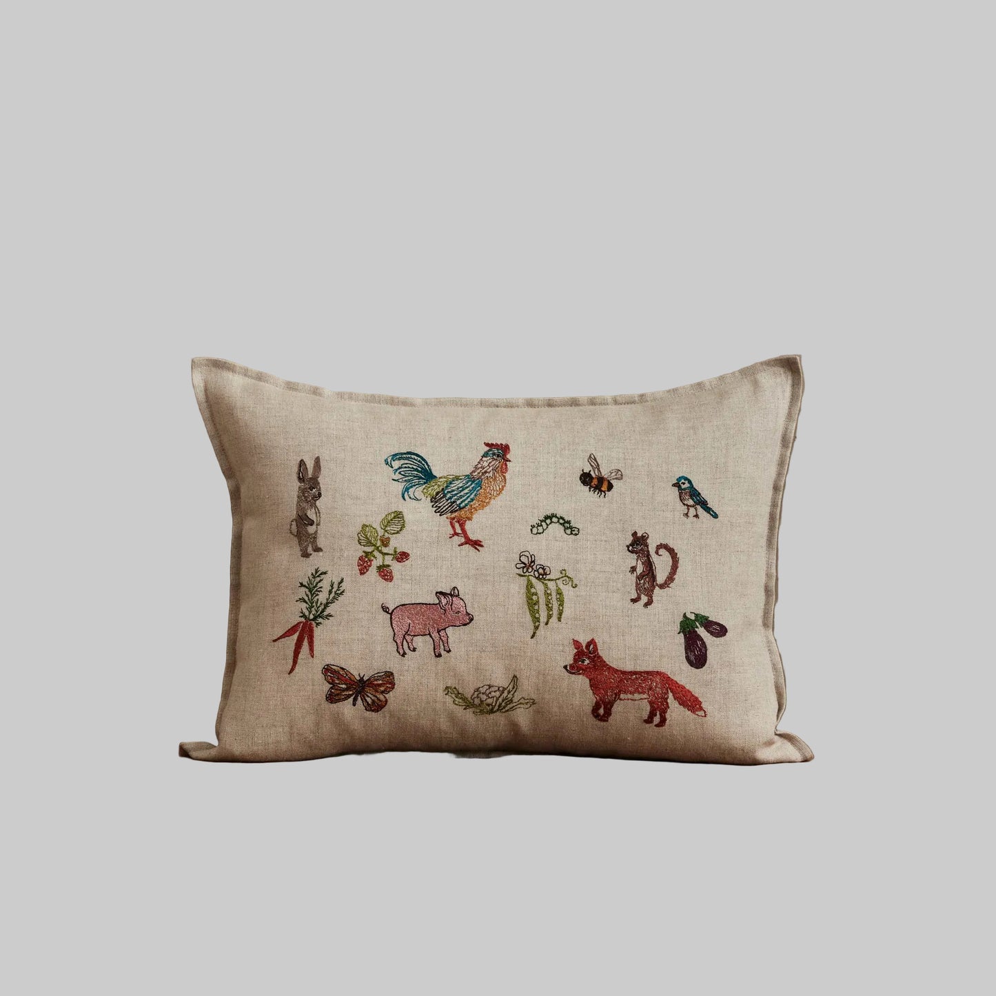 Coral and Tusk’s “Garden Gathering” embroidered linen pillow featuring colorful farm animals among pollinators, fruits, and vegetables, measures 12” x 16”