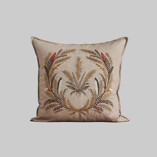 Coral and Tusk’s “Wheat Harvest” embroidered linen pillow featuring a wreath of wild grasses, grains, stalks of wheat, and found feathers, measures 20” x 20”