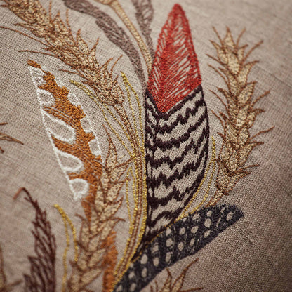 Coral and Tusk’s “Wheat Harvest” embroidered linen pillow featuring a wreath of wild grasses, grains, stalks of wheat, and found feathers, measures 20” x 20”