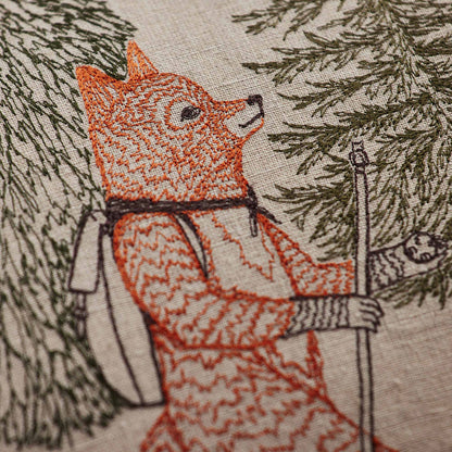 Coral and Tusk’s “Hikers” embroidered linen pillow featuring woodland friends trekking through the wilderness, measures 14” x 26”