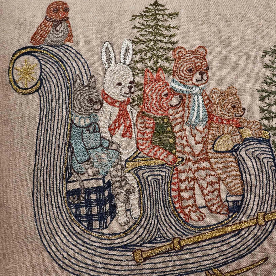 Coral and Tusk's "Jingle Bells" embroidered linen pillow featuring a design of forest friends riding though the woods on a sleigh