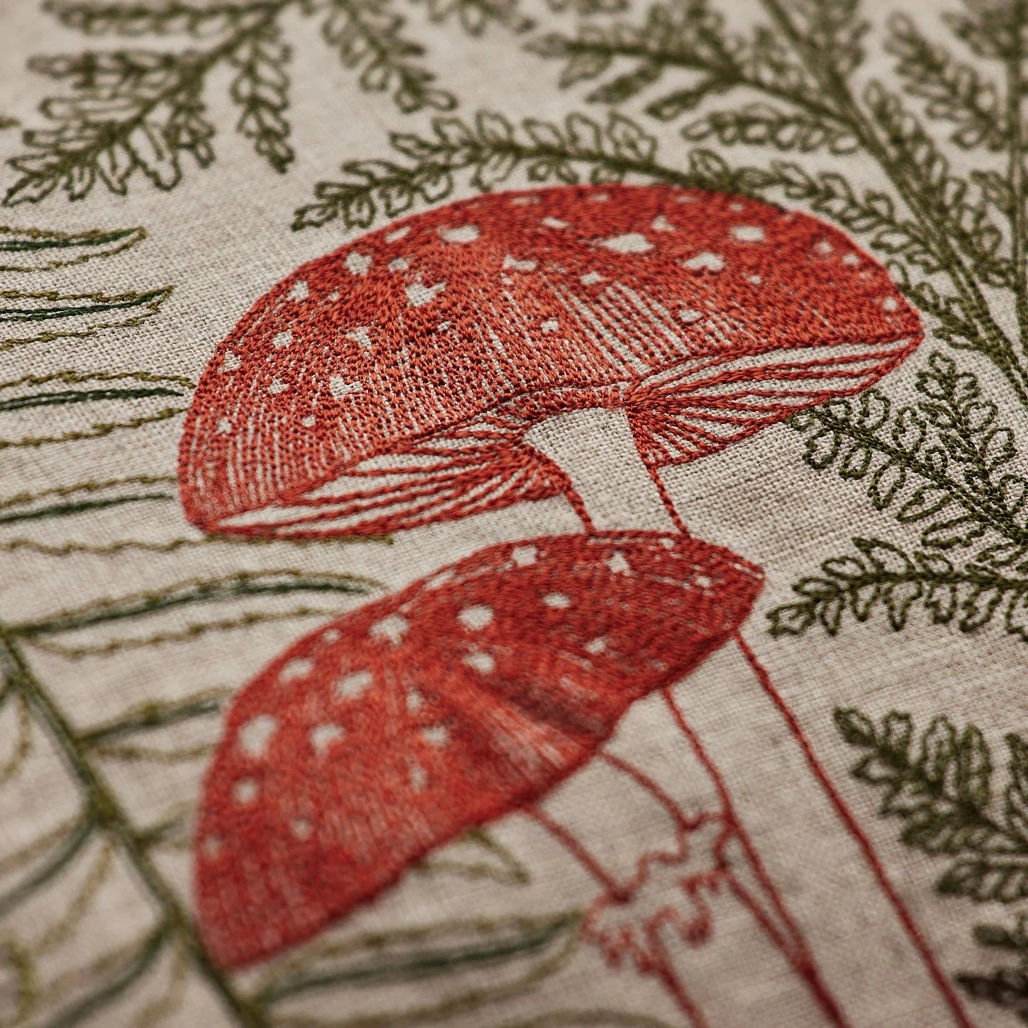 Coral and Tusk’s “Mushrooms and Ferns” embroidered linen lumbar pillow featuring a shade garden of ferns intertwined with a treasure trove of mushrooms, measures 16” x 32”