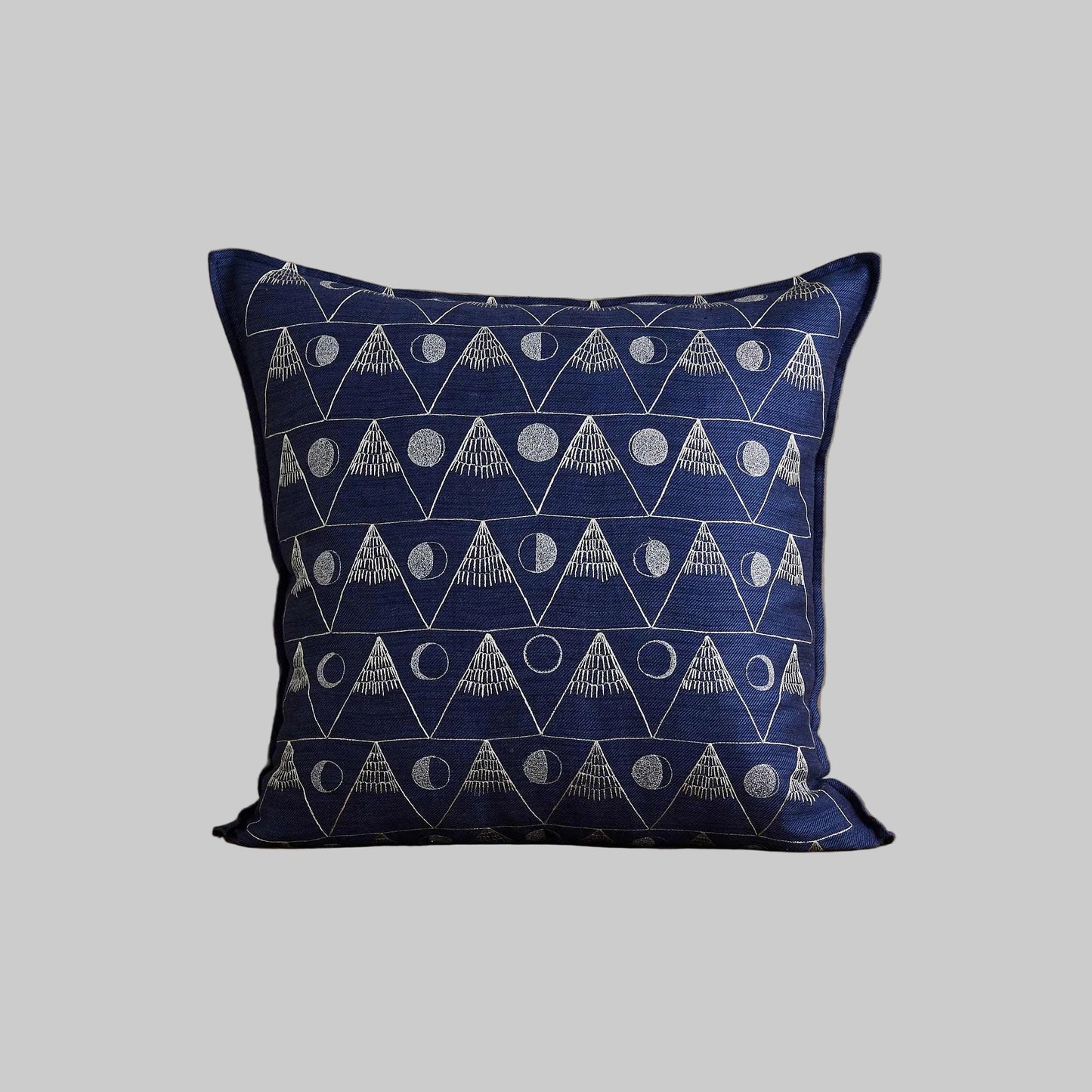 Coral and Tusk’s “Moon Mountain” embroidered indigo linen pillow featuring the lunar cycle as the moon waxes and wanes between snowy peaked mountains, measuring 20” x 20”