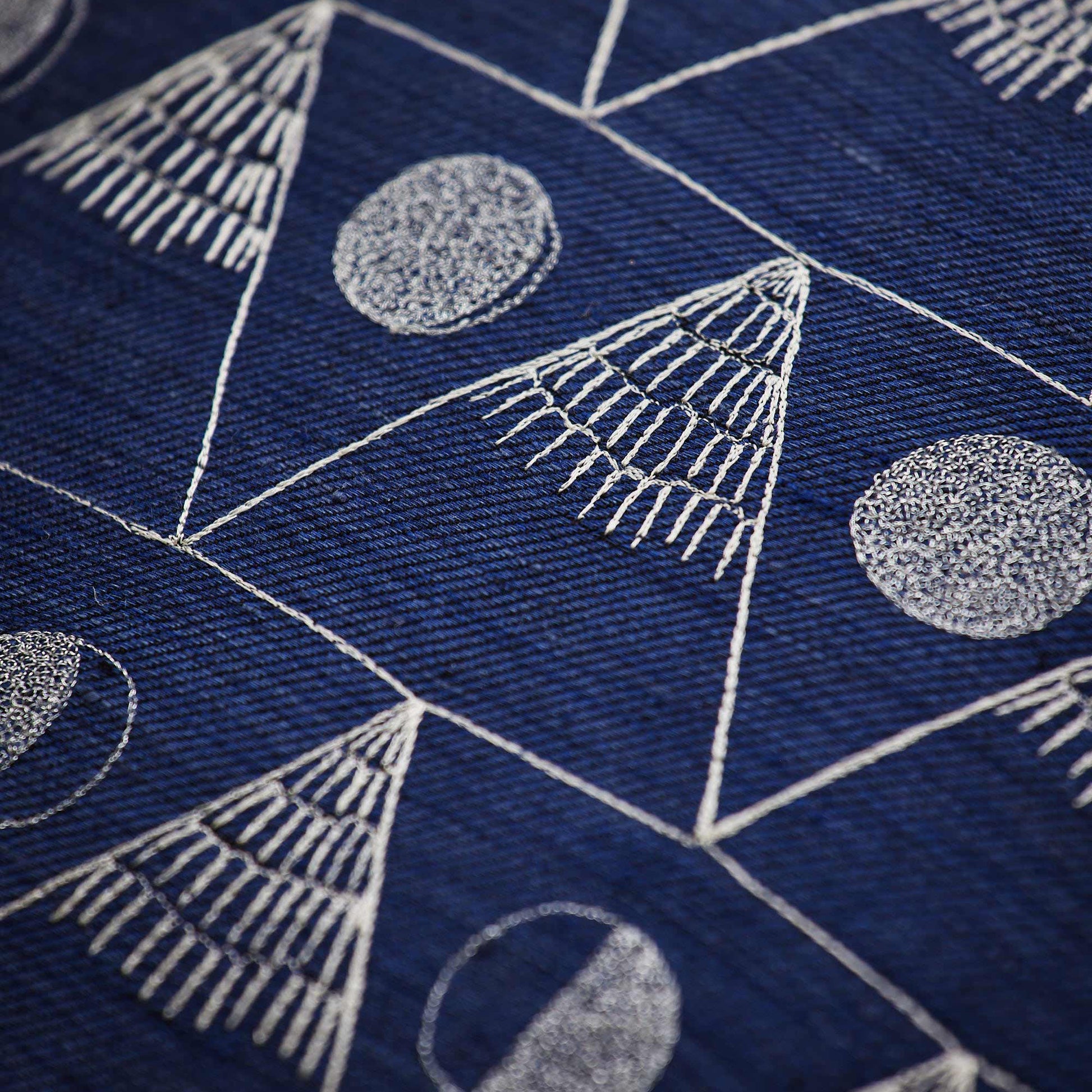 Coral and Tusk’s “Moon Mountain” embroidered indigo linen pillow featuring the lunar cycle as the moon waxes and wanes between snowy peaked mountains, measuring 20” x 20”