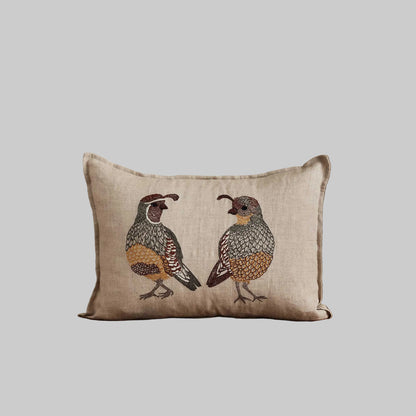 Coral and Tusk’s “Desert Quail Love” embroidered linen pillow featuring a pair of quails with gold, brown, and gray feathers, measures 12” x 16”