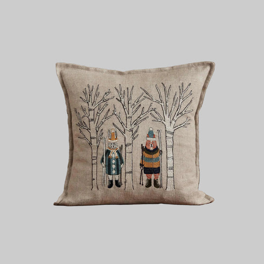 Coral and Tusk’s “Aspen Skiers” embroidered linen pillow featuring fox and bunny skiers standing amongst aspen trees, measures 12” x 12”