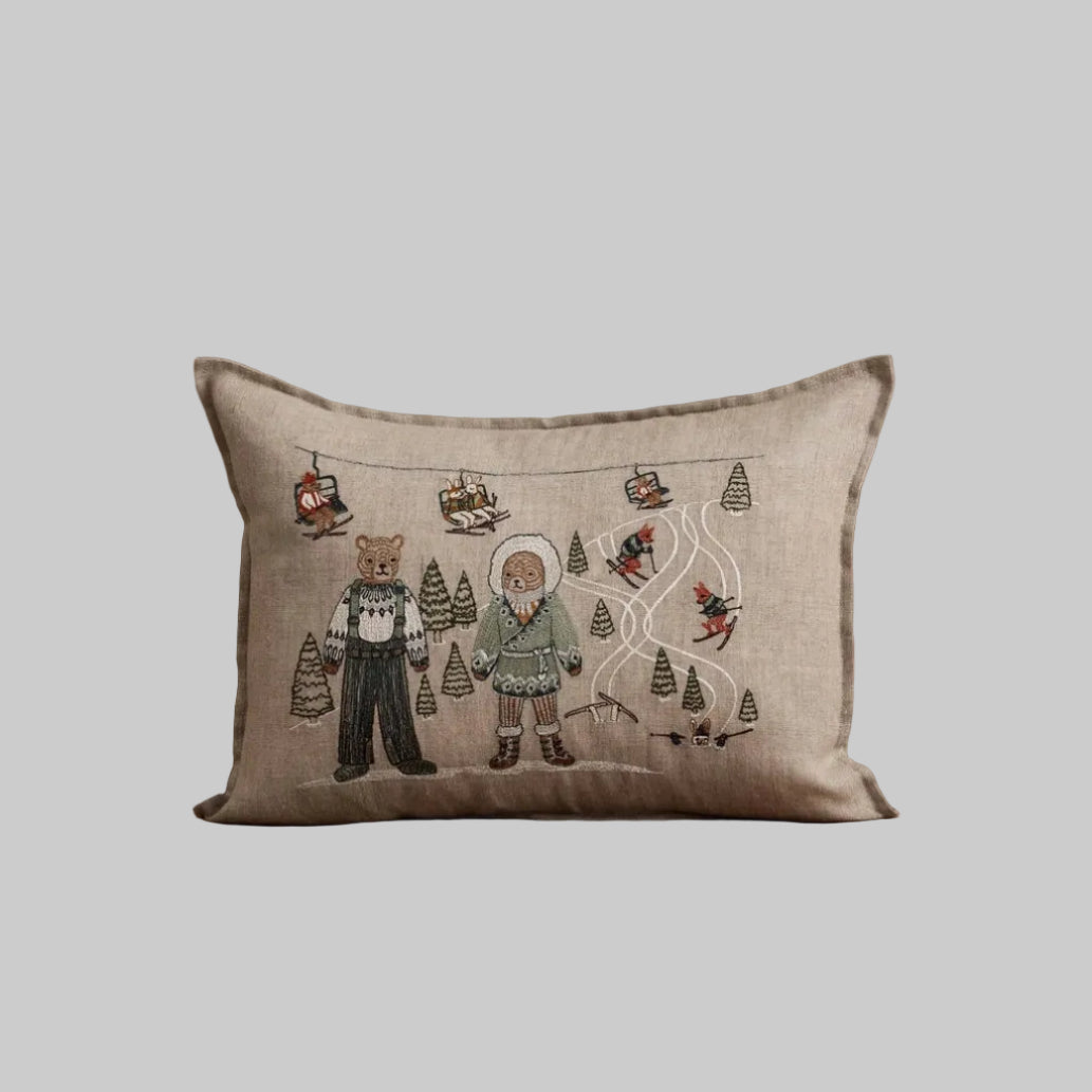 Coral and Tusk's "Ski Slope" embroidered  linen pillow featuring a design of two bears enjoying a day of skiing in coordinating cozy outfits
