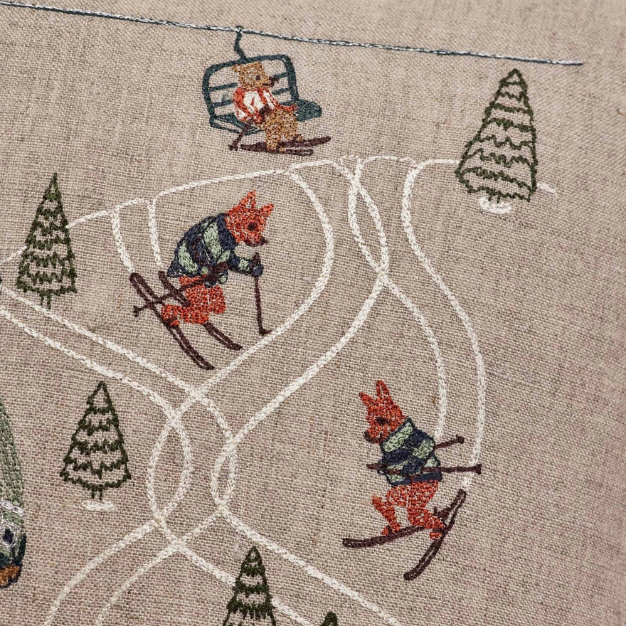 Coral and Tusk's "Ski Slope" embroidered  linen pillow featuring a design of two bears enjoying a day of skiing in coordinating cozy outfits