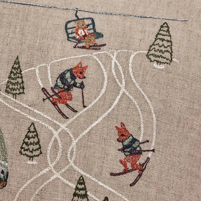 Coral and Tusk's "Ski Slope" embroidered  linen pillow featuring a design of two bears enjoying a day of skiing in coordinating cozy outfits