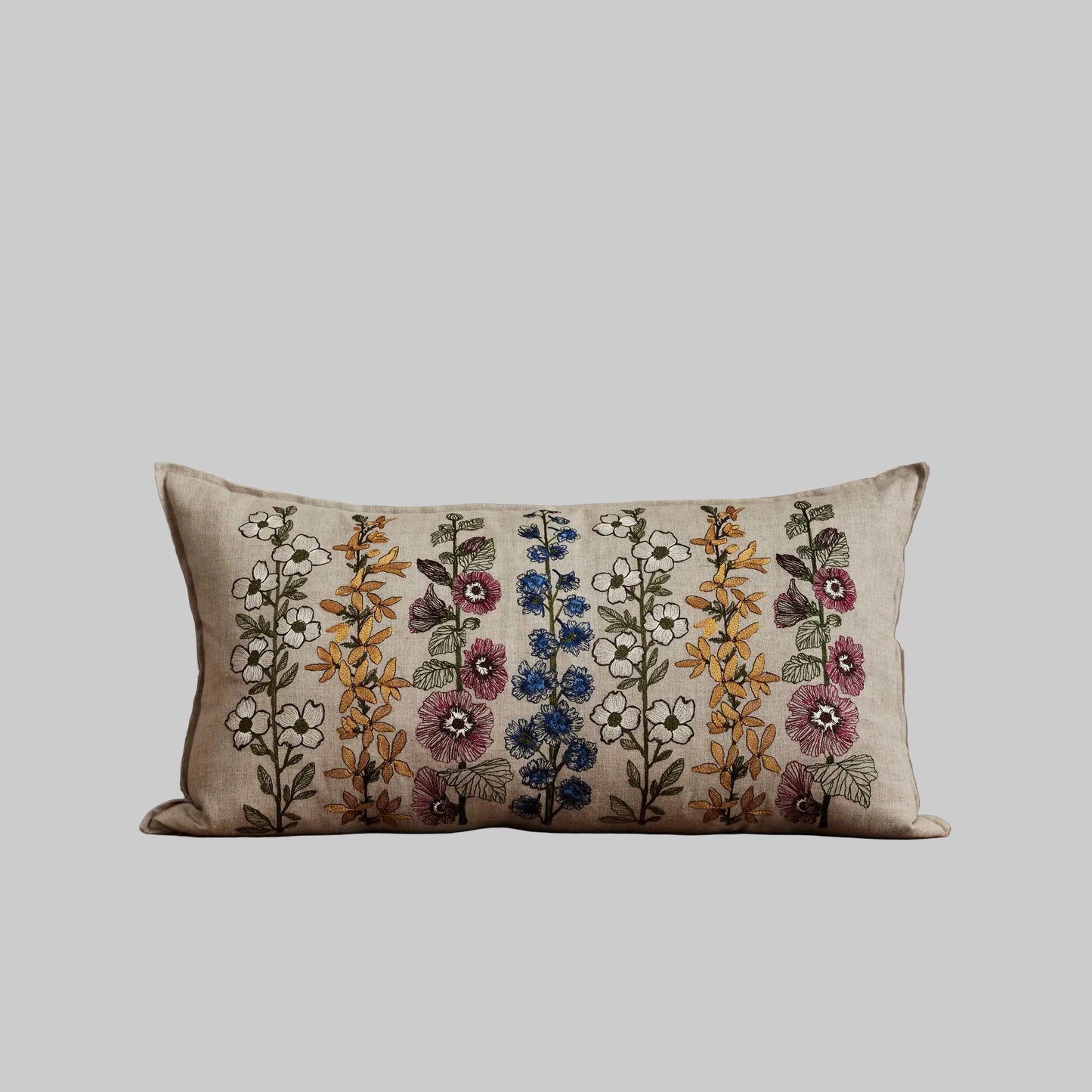Coral and Tusk’s “Spring Stems” embroidered linen pillow featuring intricate delphiniums, dogwoods, forsythia, and hollyhocks, measures 14” x 26”