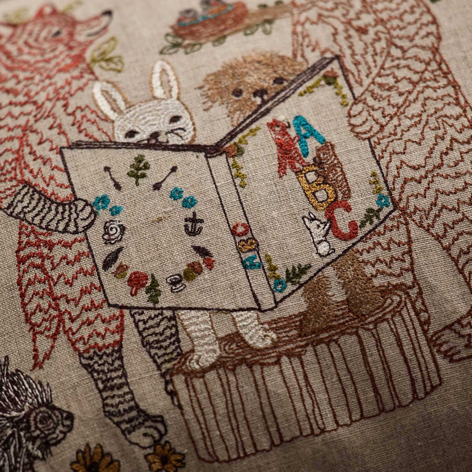 Coral and Tusk’s “Storytime” embroidered linen pillow featuring woodland animal friends gathered around listening to an A-B-C book be read aloud 