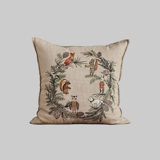 Coral and Tusks “Tree Trimmers Wreath” embroidered linen pillow featuring animal friends ushering in the holidays by decorating an evergreen wreath, measures 20” x 20”