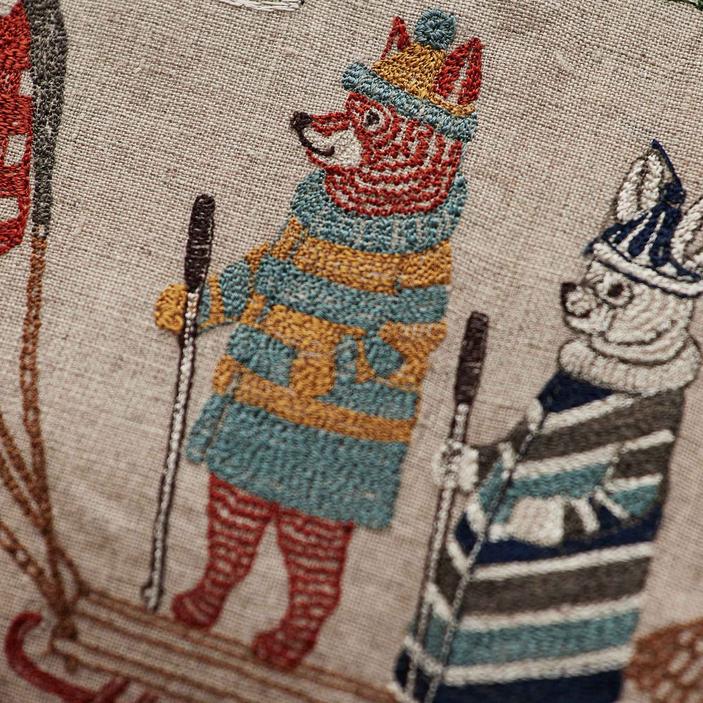 Coral and Tusk’s “Winter Fun” embroidered linen pillow featuring woodland animals in sweaters ushering in the winter solstice by sledding and skiing, measures 20” x 20”