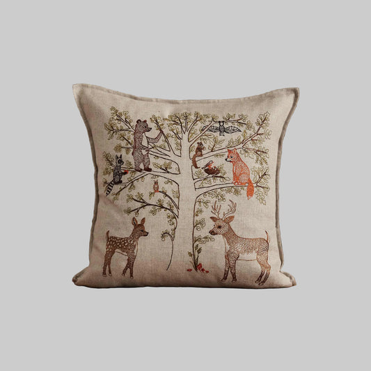 Coral and Tusk’s “Woodland Living Tree” embroidered linen pillow featuring a bear, raccoon, bird, fox, and deer living among towering trees and tiny mushrooms, measures 16” x 16”