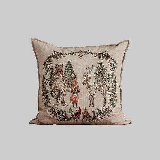 Coral and Tusk’s “Christmas Cheer Wreath” embroidered linen pillow featuring woodland dwellers framed by an evergreen wreath with pinecones and cardinals, measures 20” x 20”