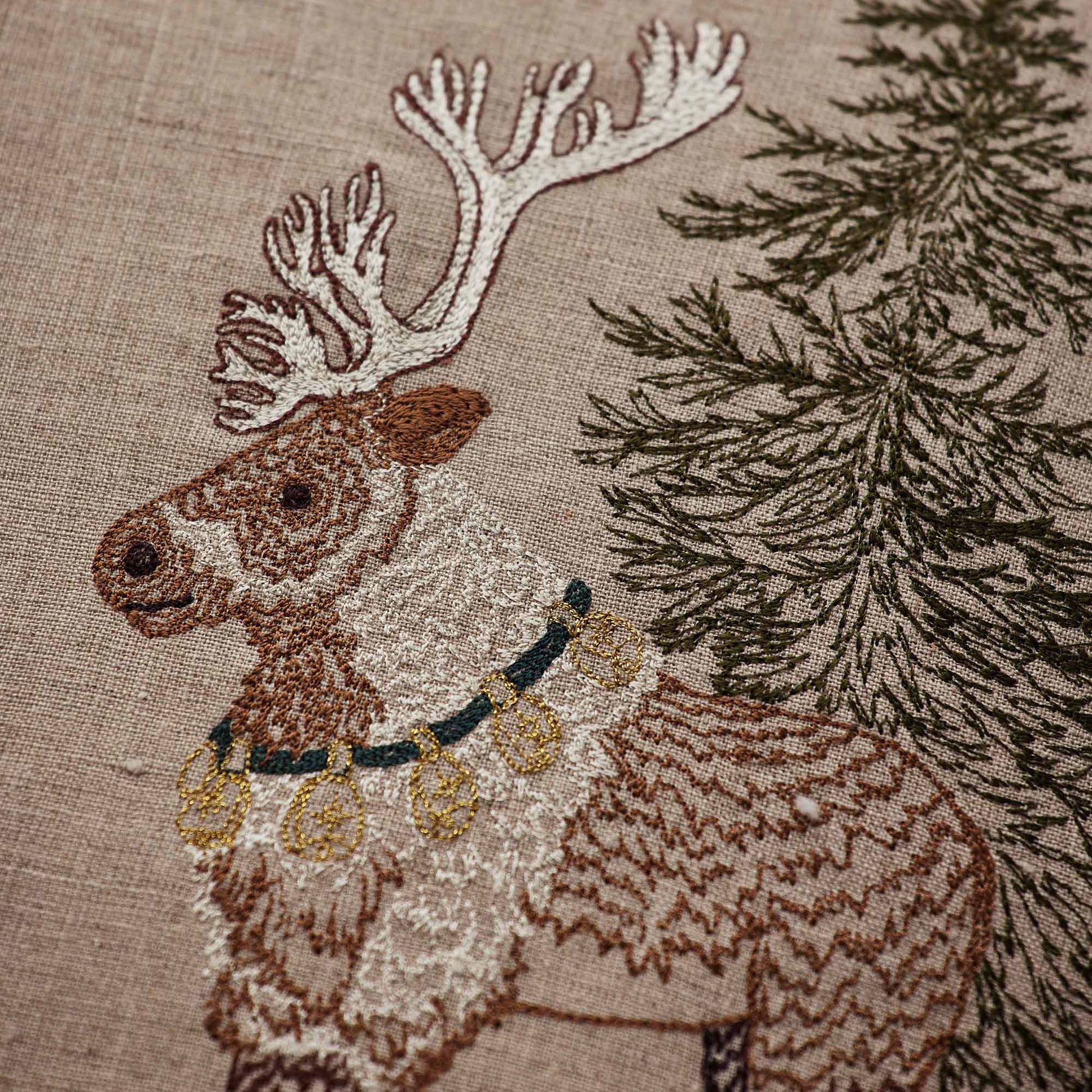 Coral and Tusk’s “Christmas Cheer Wreath” embroidered linen pillow featuring woodland dwellers framed by an evergreen wreath with pinecones and cardinals, measures 20” x 20”