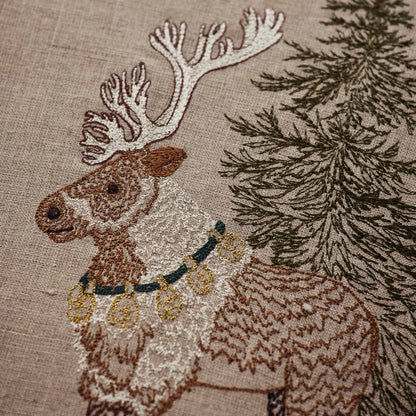 Coral and Tusk’s “Christmas Cheer Wreath” embroidered linen pillow featuring woodland dwellers framed by an evergreen wreath with pinecones and cardinals, measures 20” x 20”