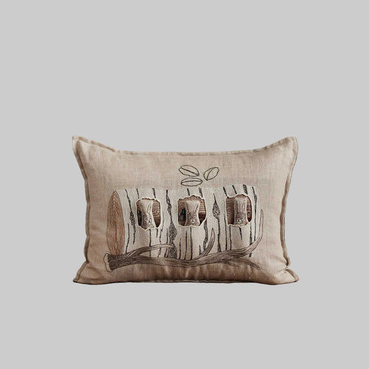 Coral and Tusk’s “Aspen Log Bunnies” embroidered linen pocket pillow featuring a family of three rabbits hiding away in their cozy tree stump home, measures 12” x 16”