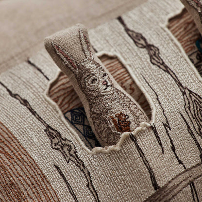 Coral and Tusk’s “Aspen Log Bunnies” embroidered linen pocket pillow featuring a family of three rabbits hiding away in their cozy tree stump home, measures 12” x 16”