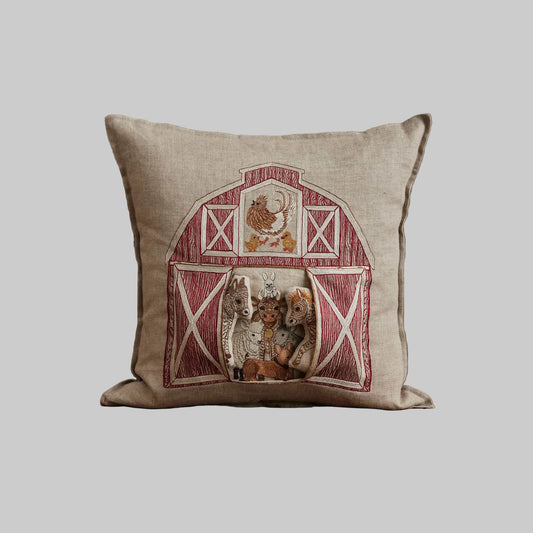 Coral and Tusk’s “Red Barn” embroidered linen pocket pillow featuring a farm scene with several barnyard animals, measures 16” x 16”
