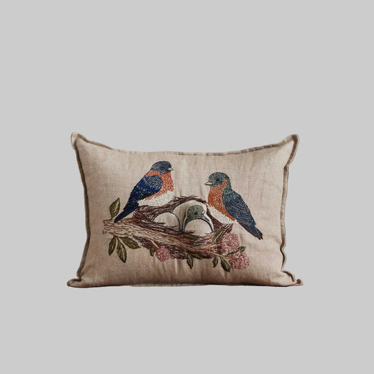Coral and Tusk’s “Bluebird Nest” embroidered linen pocket pillow featuring a family of bluebirds in a cherry blossom tree, measures 12” x 16”