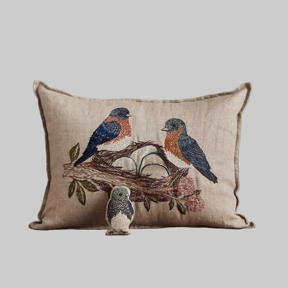 Coral and Tusk’s “Bluebird Nest” embroidered linen pocket pillow featuring a family of bluebirds in a cherry blossom tree, measures 12” x 16”