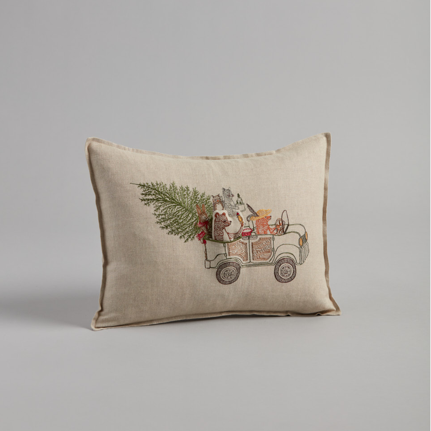Coral and Tusk's "Christmas Tree Car" embroidered linen pocket pillow featuring woodland animals riding in a car with their Christmas tree, measures 12" x 16"