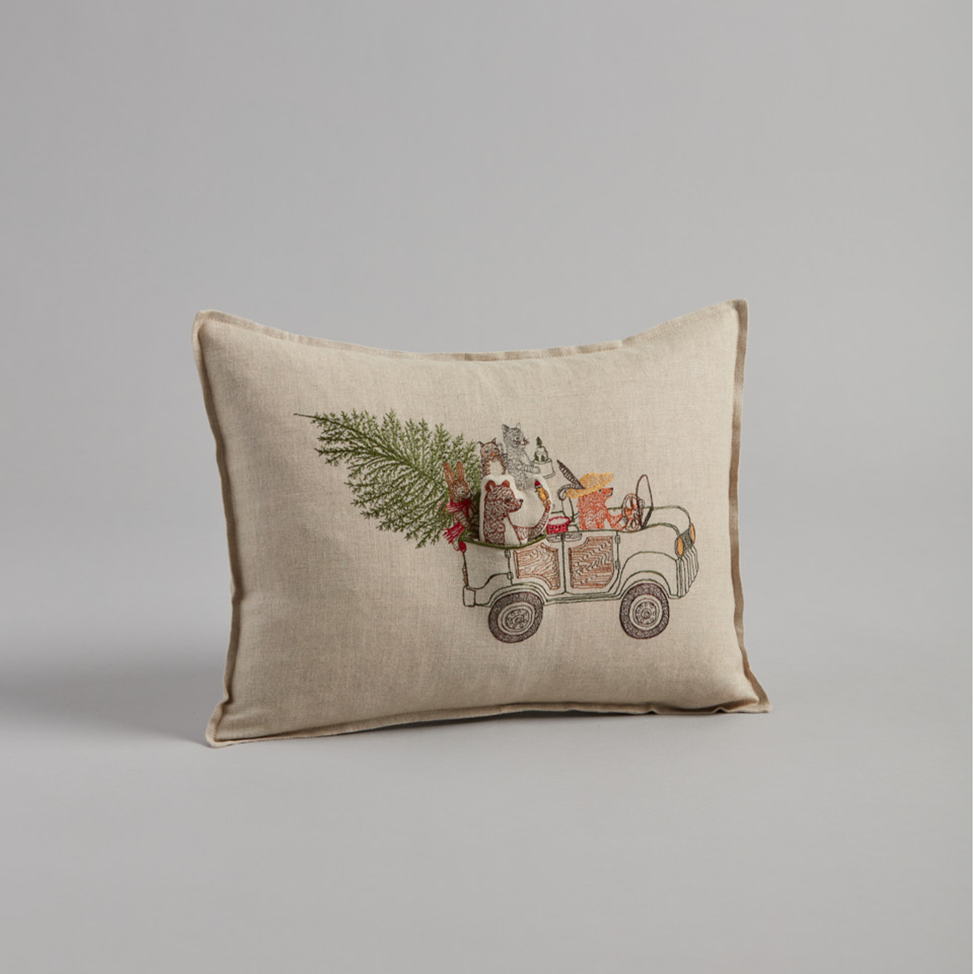 Coral and Tusk's "Christmas Tree Car" embroidered linen pocket pillow featuring woodland animals riding in a car with their Christmas tree, measures 12" x 16"
