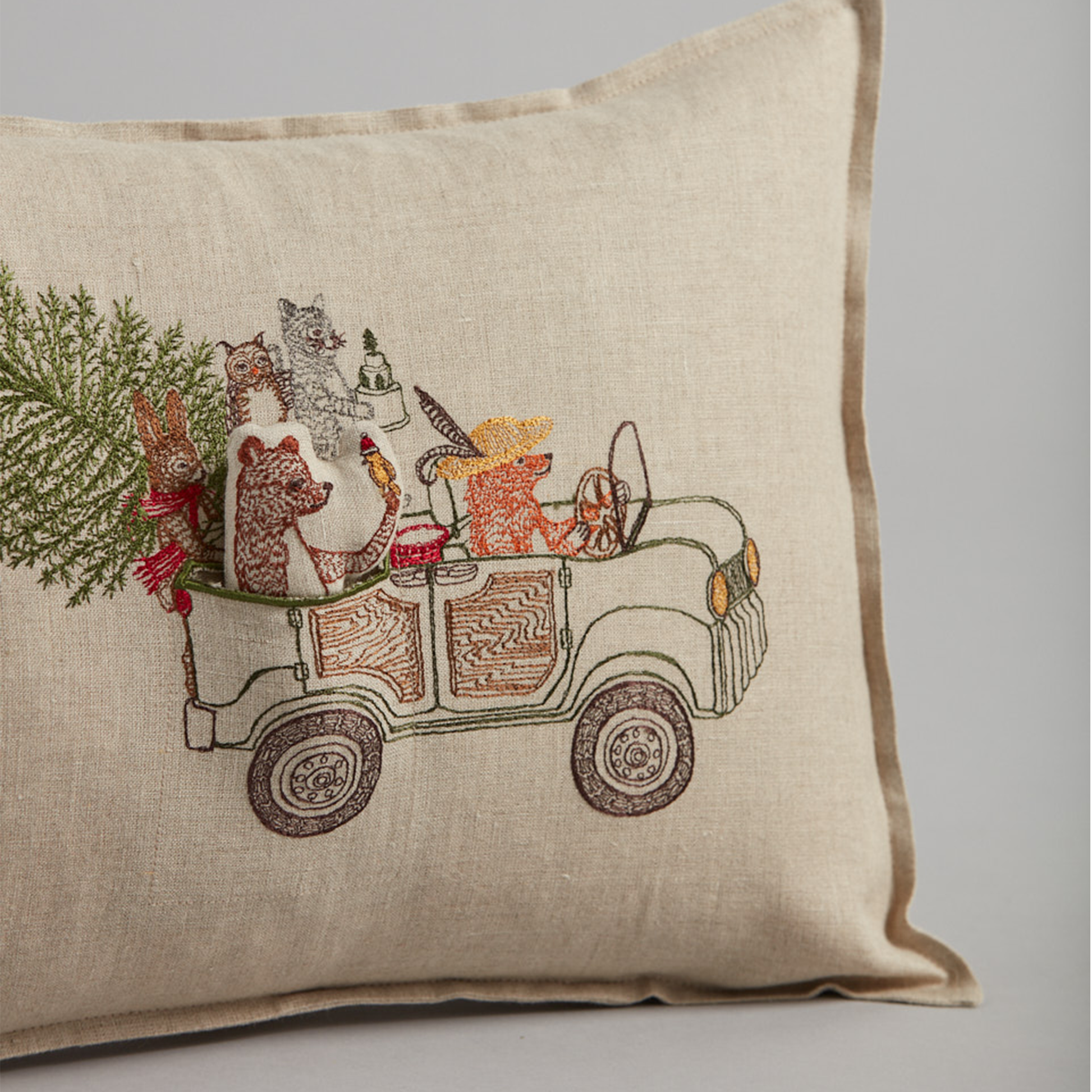 Coral and Tusk's "Christmas Tree Car" embroidered linen pocket pillow featuring woodland animals riding in a car with their Christmas tree, measures 12" x 16"