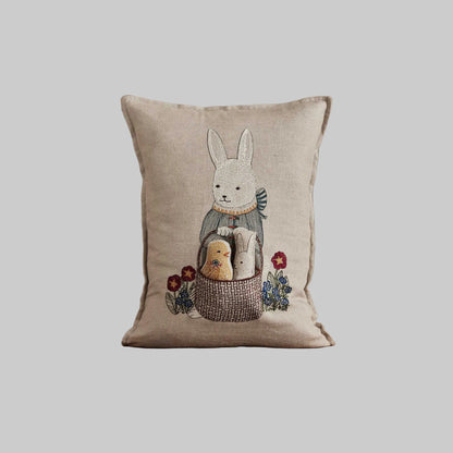 Coral and Tusk’s “Easter Bunny” embroidered linen pocket pillow featuring a festive rabbit carrying a basket with a chick and bunny inside, measures 12“ x 16”