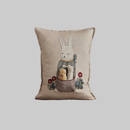 Coral and Tusk’s “Easter Bunny” embroidered linen pocket pillow featuring a festive rabbit carrying a basket with a chick and bunny inside, measures 12“ x 16”