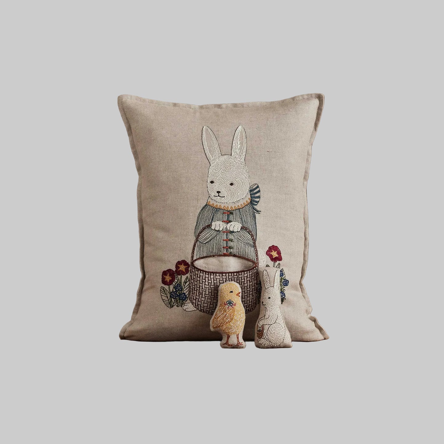 Coral and Tusk’s “Easter Bunny” embroidered linen pocket pillow featuring a festive rabbit carrying a basket with a chick and bunny inside, measures 12“ x 16”