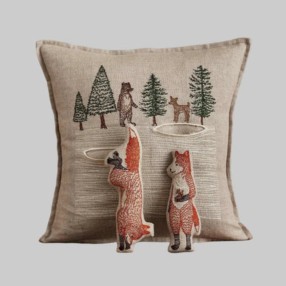 Coral and Tusk’s “Winter Foxes” embroidered linen pocket pillow featuring two foxes in the middle of a hunt, measures 12” x 12”