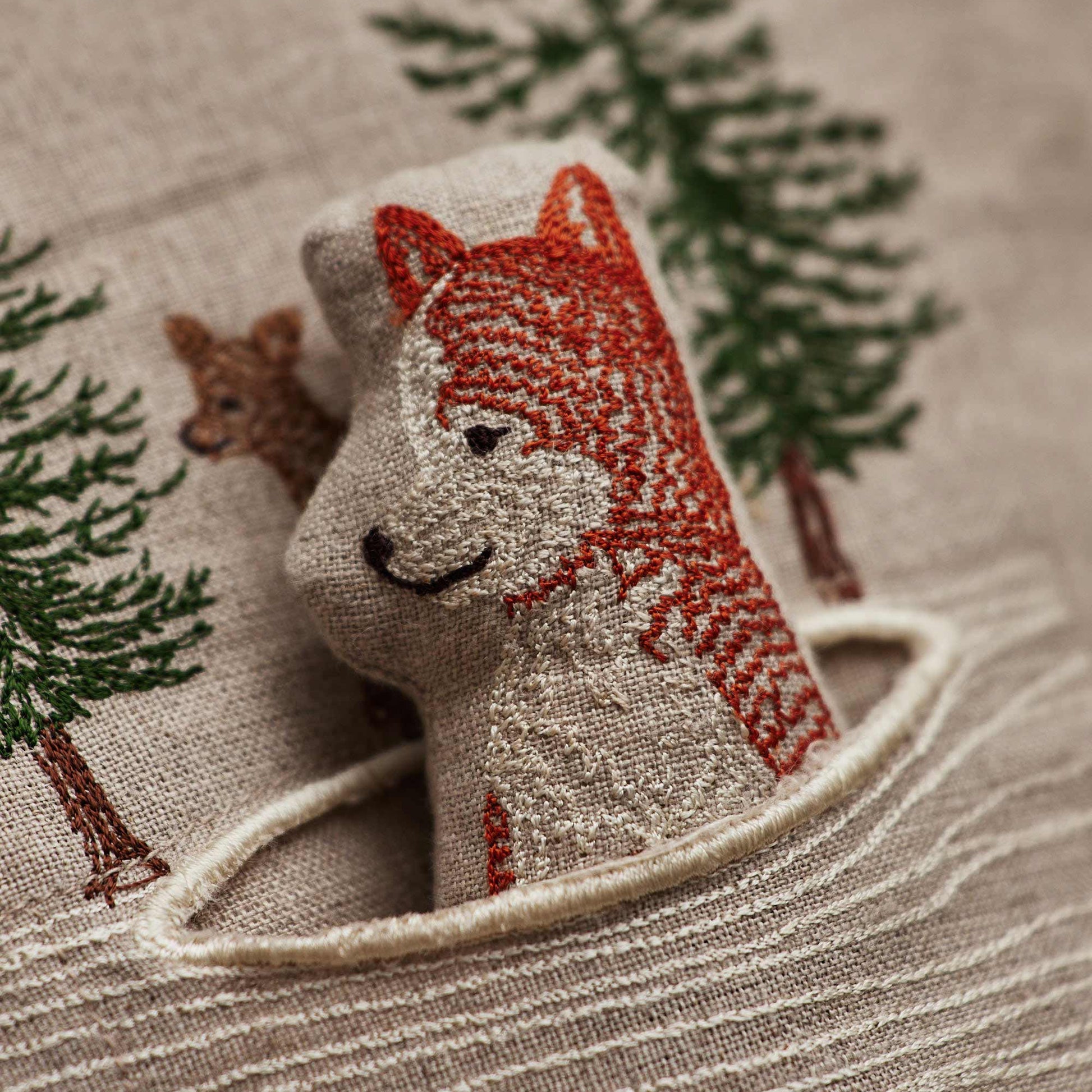 Coral and Tusk’s “Winter Foxes” embroidered linen pocket pillow featuring two foxes in the middle of a hunt, measures 12” x 12”