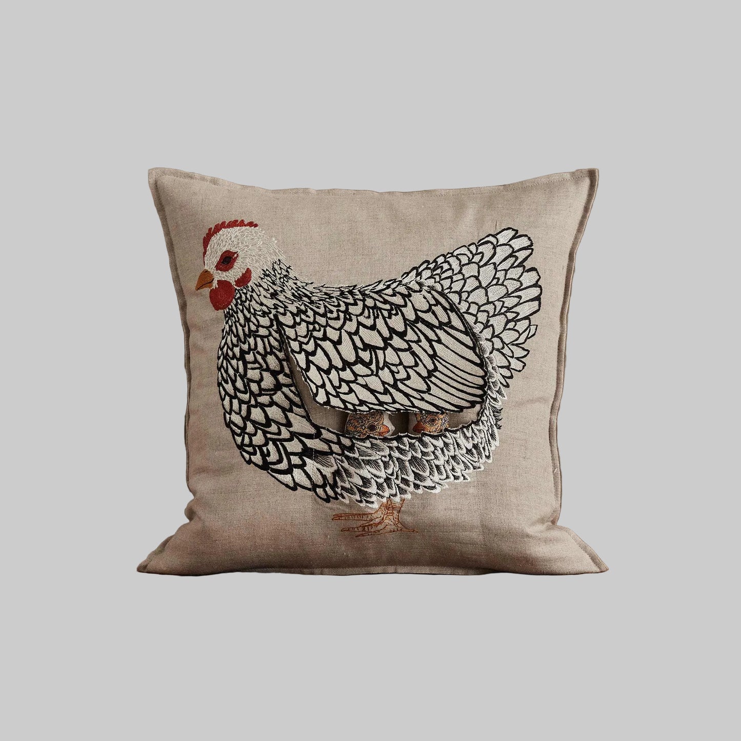 Coral and Tusk’s “Mother Hen” embroidered linen pocket pillow featuring a mother chicken with removable chicks under her wing, measures 16” x 16”