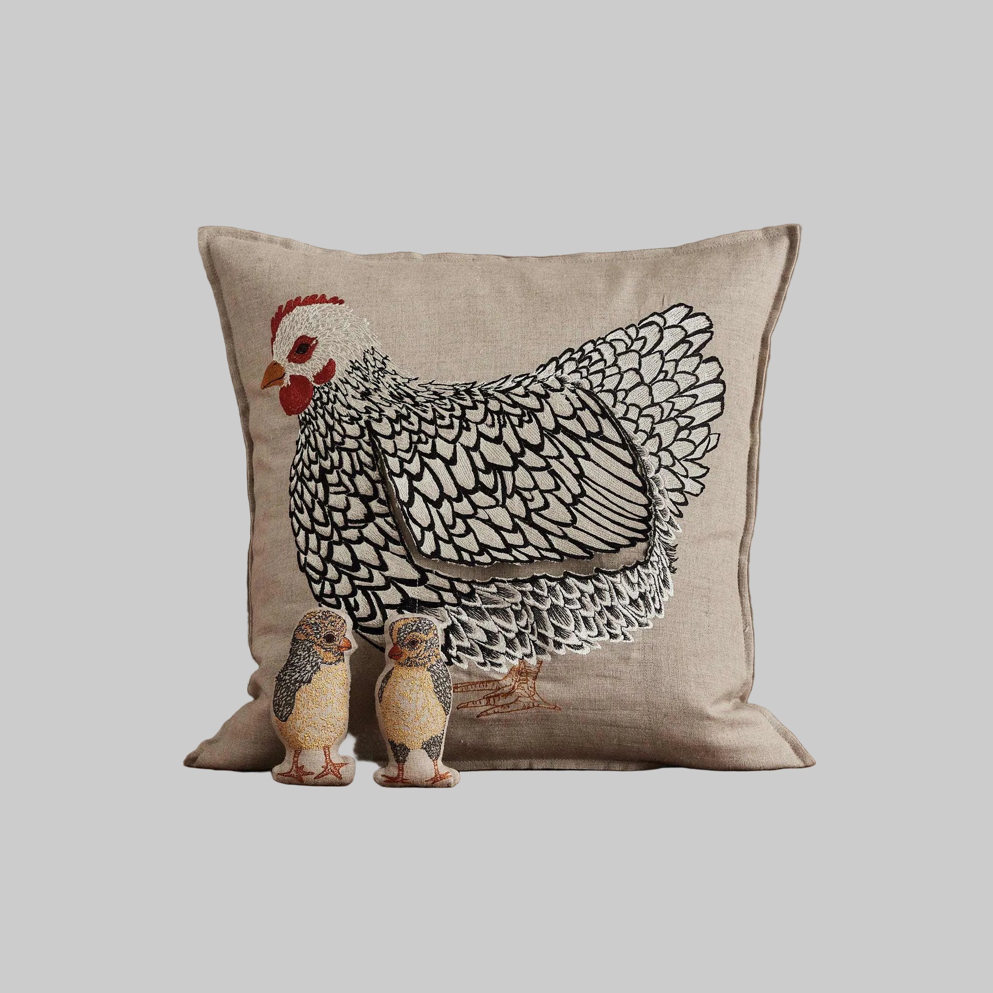 Coral and Tusk’s “Mother Hen” embroidered linen pocket pillow featuring a mother chicken with removable chicks under her wing, measures 16” x 16”