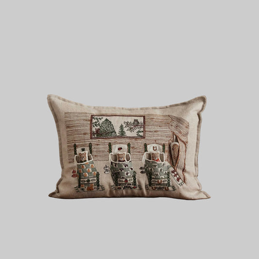 Coral and Tusk’s “Three Little Bears” embroidered linen pocket pillow featuring three bears tucked in bed with a puppy hiding in the doorway, measures 12” x 16”