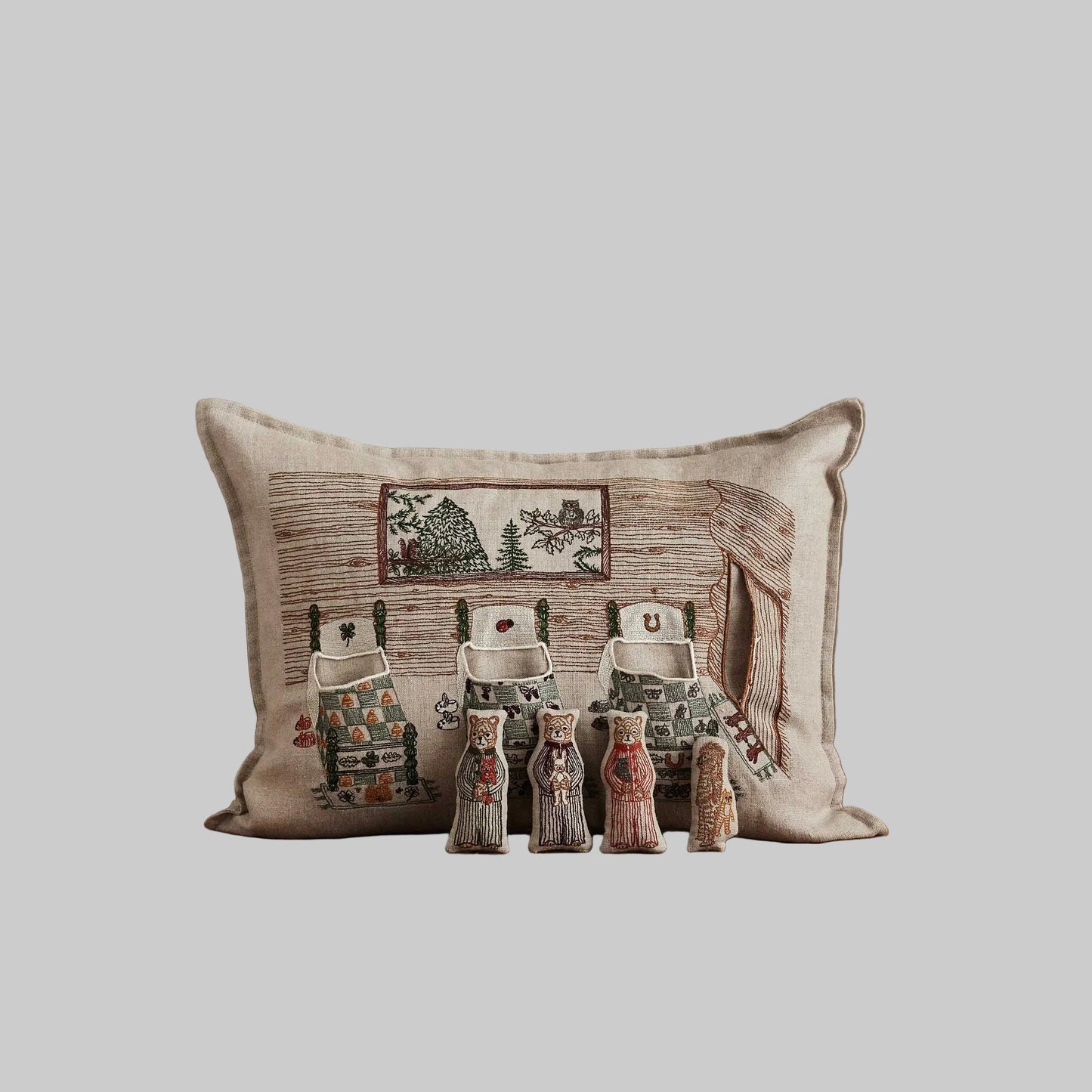 Coral and Tusk’s “Three Little Bears” embroidered linen pocket pillow featuring three bears tucked in bed with a puppy hiding in the doorway, measures 12” x 16”